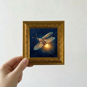 Puede incluir: Una peque&ntilde;a pintura cuadrada en un marco dorado representa una luci&eacute;rnaga sobre un fondo azul oscuro. La luci&eacute;rnaga tiene alas transl&uacute;cidas y un abdomen brillante. El marco tiene un dise&ntilde;o ornamentado y texturizado.
