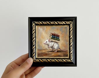 May include: A framed painting depicts a white mouse carrying a stack of books on its back. The mouse holds a small paper in its front paws. The painting is in a black frame with gold accents. The background is a warm, neutral color.