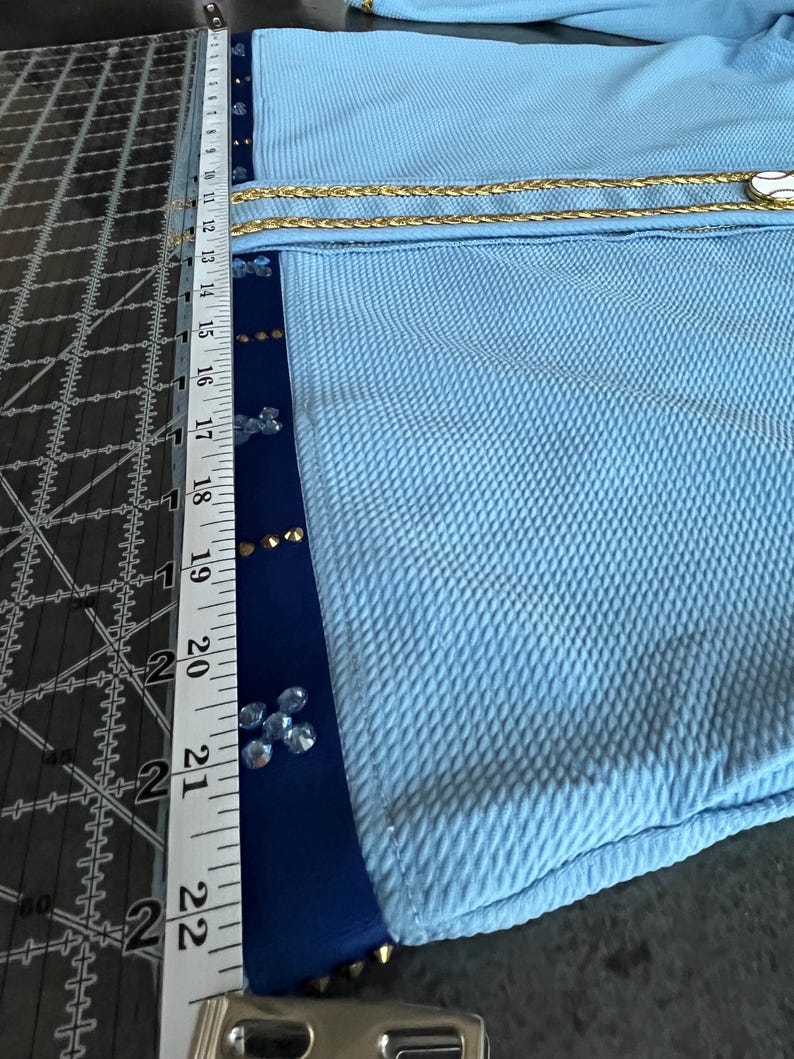 May include: A light blue fabric with a gold chain trim and blue trim with rhinestones. The fabric is measured with a ruler that shows 22 inches.