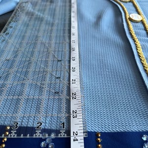May include: A light blue blazer with a gold trim and blue ribbon detail. The blazer has a textured fabric and is decorated with gold buttons and rhinestones.