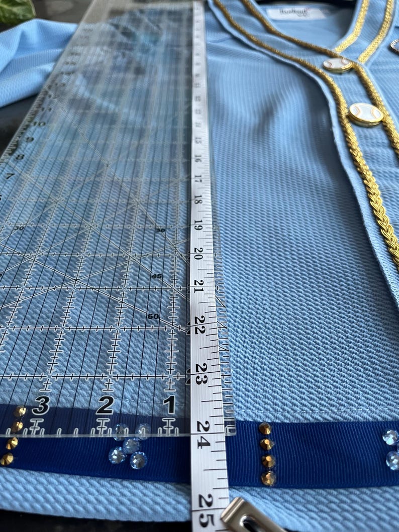 May include: A light blue blazer with a gold trim and blue ribbon detail. The blazer has a textured fabric and is decorated with gold buttons and rhinestones.