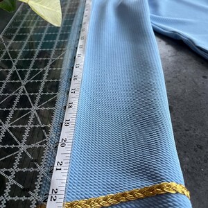 May include: A light blue fabric with a gold braid trim. The fabric is measured with a ruler that shows 23 inches.