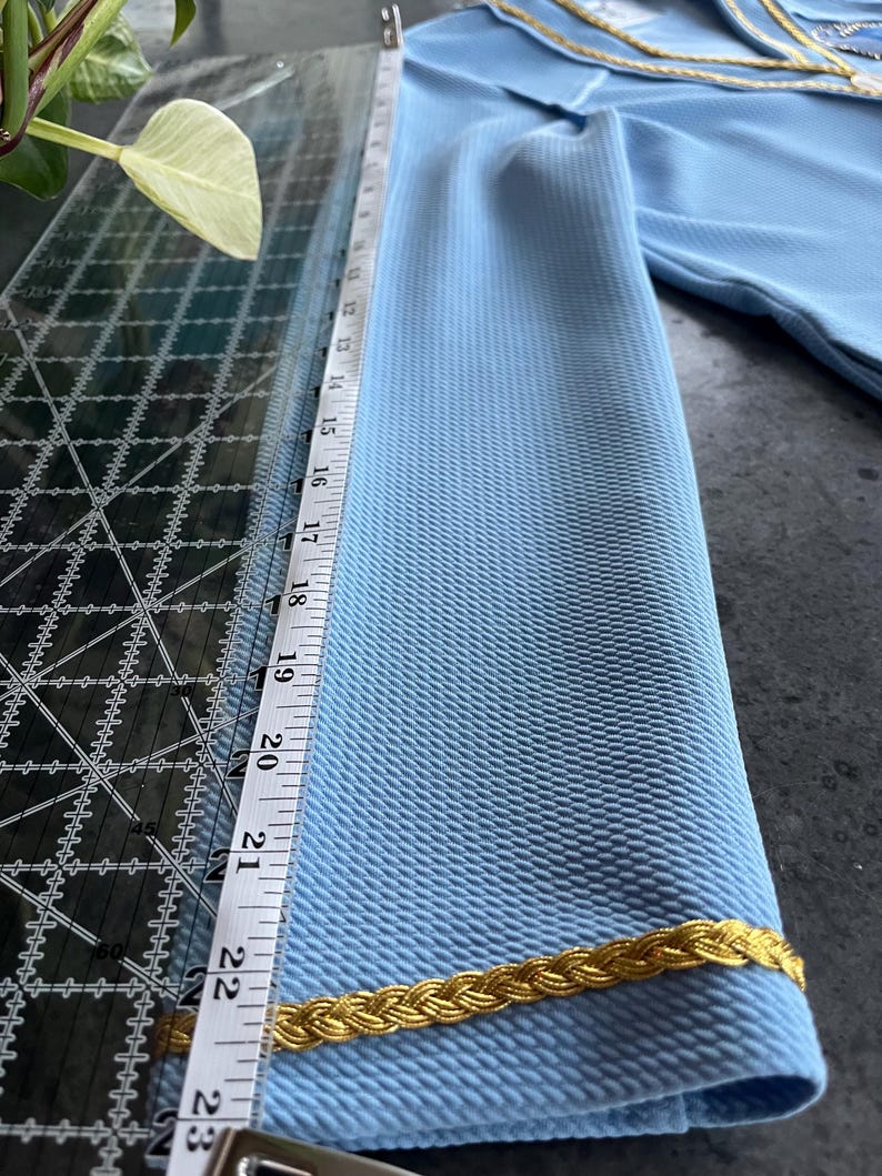 May include: A light blue fabric with a gold braid trim. The fabric is measured with a ruler that shows 23 inches.