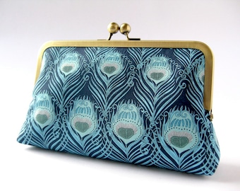 May include: A blue and teal clutch purse with a peacock feather pattern and a gold clasp.