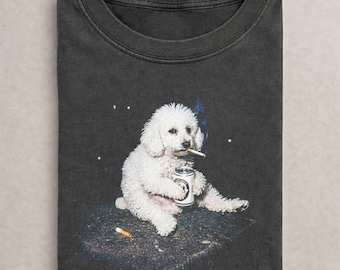 May include: A charcoal gray crew neck t-shirt featuring a graphic print of a white poodle sitting down, holding a silver beverage can, and holding a lit cigarette in its mouth. A second cigarette lies on the dark surface below the dog.