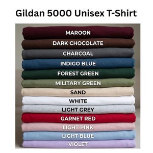 May include: A stack of Gildan 5000 unisex t-shirts in various colors including maroon, dark chocolate, charcoal, indigo blue, forest green, military green, sand, white, light grey, garnet red, light pink, light blue, and violet, labeled by color.