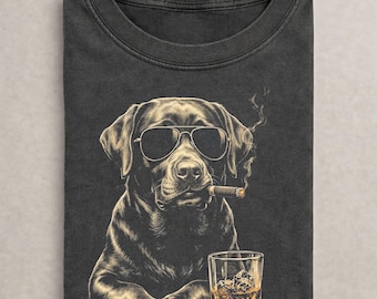 May include: A charcoal gray t-shirt featuring a graphic illustration of a black Labrador retriever wearing dark sunglasses, holding a lit cigar in its mouth, and positioned next to a glass of amber-colored liquid with ice cubes inside.