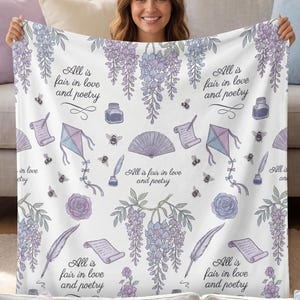 May include: A white throw blanket with a floral and literary design. The blanket features illustrations of wisteria, bees, kites, scrolls, and the text "All is fair in love and poetry" in a soft purple and blue colour palette.