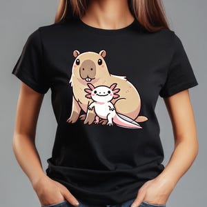 Pode incluir: Uma camiseta preta com uma imagem de desenho animado de uma capivara e uma axolotl. A capivara &eacute; marrom e tem o nariz rosa. A axolotl &eacute; rosa e tem a barriga branca.