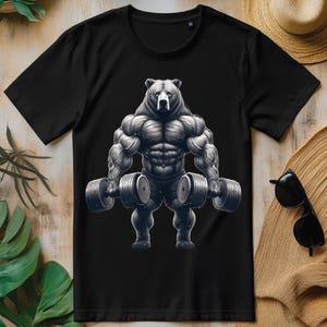 Puede incluir: Camiseta negra con un gráfico de un oso musculoso levantando pesas. El oso tiene una expresión seria y lleva pantalones cortos negros.