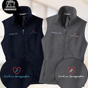 Könnte beinhalten: Zwei bestickte Fleece-Westen, eine marineblaue und eine graue. Jede Weste hat einen Reißverschluss, eine kleine Herzgrafik und den Text "Cardiac Sonographer". Die marineblaue Weste hat den Namen "Morgan, RCS" aufgestickt. Die graue Weste hat ebenfalls den Namen "Morgan, RCS" aufgestickt.