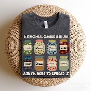 May include: Dark grey heather t-shirt with the text "INSTRUCTIONAL COACHING IS MY JAM AND I'M HERE TO SPREAD IT." The shirt features illustrations of jam jars with words like "Guide," "Inspire," and "Empower."