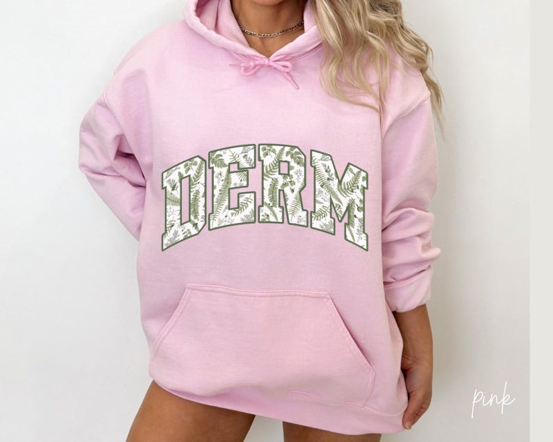 Pu&ograve; includere: Felpa rosa con stampa floreale bianca e la parola "DERM" in un grande carattere grassetto.