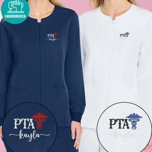 May include: Navy blue and white zip-up medical scrubs with embroidered "PTA kayla" logos. The navy blue scrub has a red logo, while the white scrub has a blue logo. The scrubs have long sleeves and pockets.