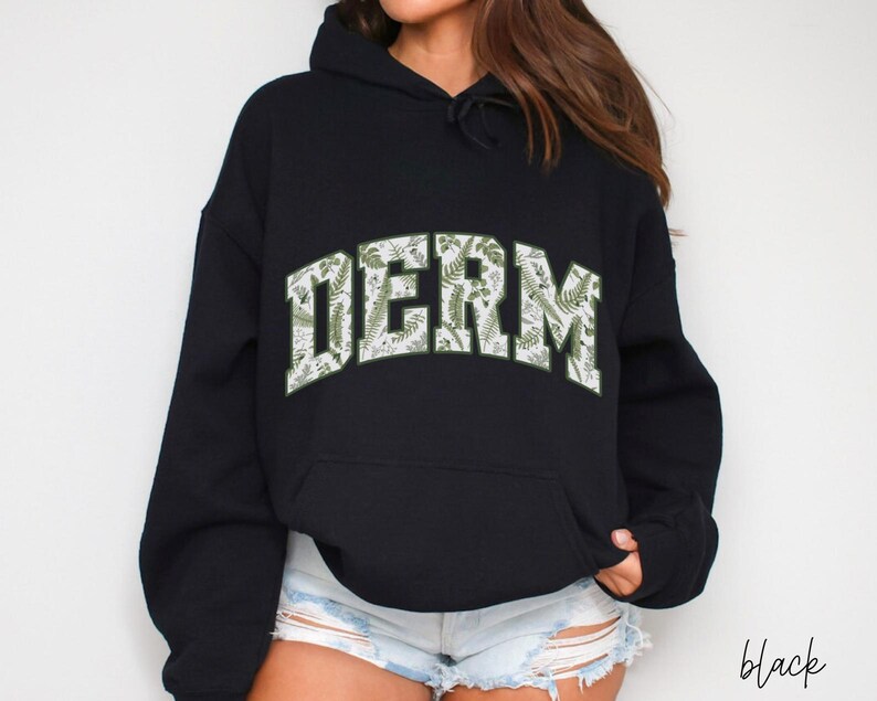 Pu&ograve; includere: Felpa con cappuccio nera con una stampa floreale bianca e verde che dice "DERM" sul davanti.