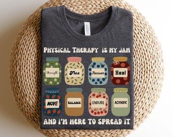 May include: Dark grey heather t-shirt with the text "PHYSICAL THERAPY IS MY JAM" and illustrated jars labeled with words like "Strength", "Flex", and "Heal". The shirt also says "AND I'M HERE TO SPREAD IT".