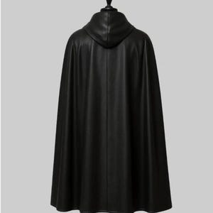 May include: A black hooded cape made of a smooth, possibly leather-like material. The cape is long, reaching to the ankles, and hangs from a black mannequin head. The back view shows the hood and the flowing fabric.