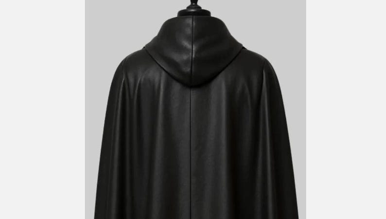 May include: A black leather cape with a hood, viewed from the back. The cape has a smooth texture and a flowing design. The hood is attached to the cape and is also made of black leather.
