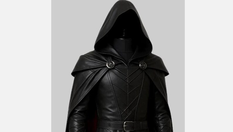 May include: A black leather hooded cloak and jacket ensemble. The cloak features a cape and is fastened with two decorative clasps. The jacket has a belt and intricate stitching details. The outfit is displayed on a mannequin.
