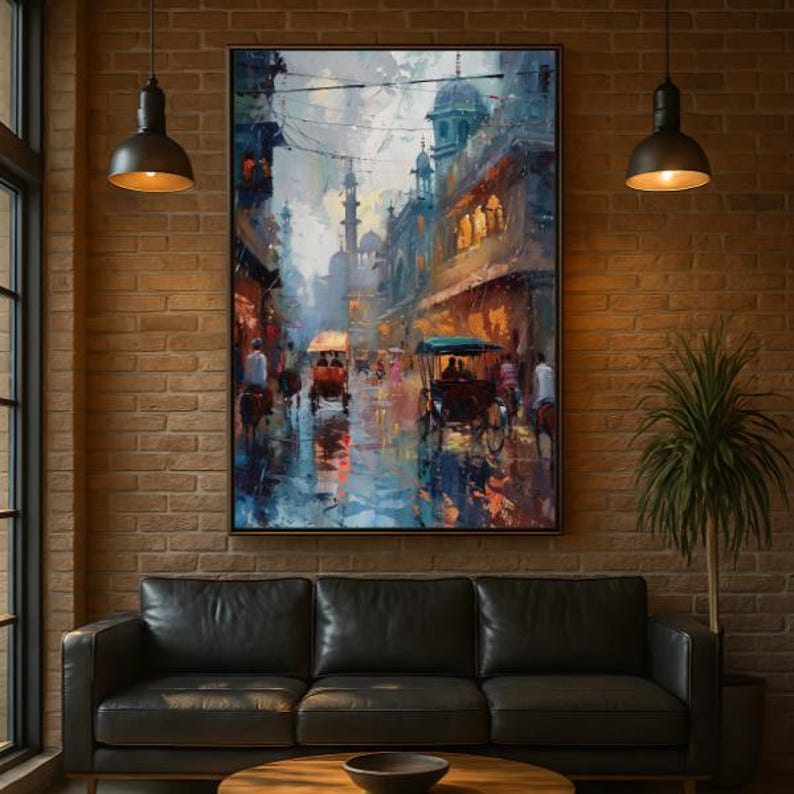 May include: An oil painting depicting a bustling street scene with rickshaws and buildings in shades of blue, orange, and brown. The artwork is framed and hangs above a black leather sofa, with a brick wall background.
