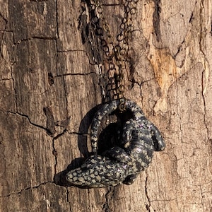 May include: A black and white speckled lizard pendant necklace with a brass chain.