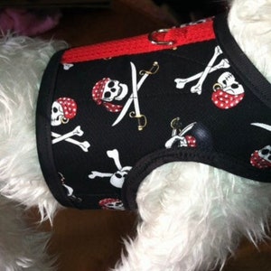 Może przedstawiać: Czarny szelki dla psa z czerwoną lamówką i wzorem pirackiej czaszki i skrzyżowanych kości. Szelki mają wzór czerwonej i białej czaszki i skrzyżowanych kości.