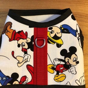 Könnte beinhalten: Weißer Hundegeschirr mit rotem Gurt und silbernem Ring. Das Geschirr zeigt ein sich wiederholendes Muster von Mickey Mouse-Charakteren in verschiedenen Posen.
