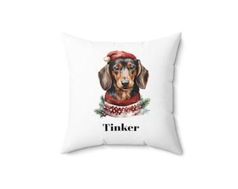 Può includere: Cuscino quadrato bianco con un'illustrazione ad acquerello di un bassotto con un cappello da Babbo Natale e un maglione rosso e bianco. La parola "Tinker" è stampata in nero sotto il cane.