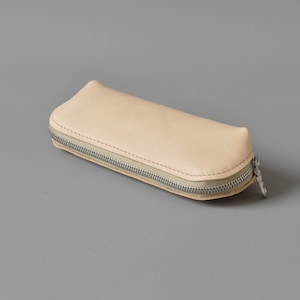 May include: A light beige leather pencil case with a zipper closure.