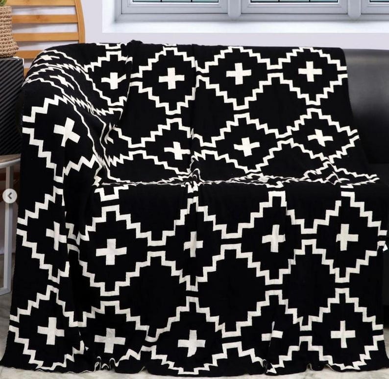 May include: Black and white throw blanket with a geometric pattern of plus signs and zigzags. The blanket is folded and draped over a black sofa.