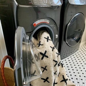 A machine washable rug, hanging out of washing machine, made out of neutraland natural raw materials, in ivory and black by rich class decor