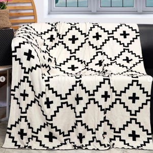 May include: A white throw blanket with a black geometric pattern of squares and crosses. The blanket is folded and draped over a couch.