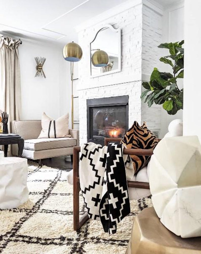 May include: A white and black patterned throw blanket draped over a wooden chair with a white cushion and a tiger print throw pillow. The chair is in front of a fireplace with a black and white patterned rug on the floor.