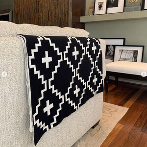 May include: A black and white throw blanket with a geometric pattern of plus signs and diamonds. The blanket is draped over a light gray couch.