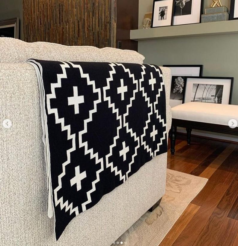 May include: A black and white throw blanket with a geometric pattern of plus signs and diamonds. The blanket is draped over a light gray couch.