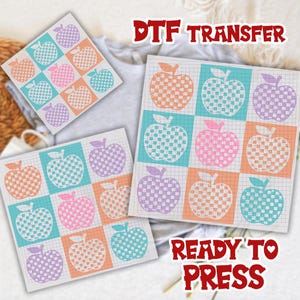 Op de afbeelding: DTF-transfervellen met een rasterpatroon van appels in verschillende kleuren. De appels zijn oranje, blauw, roze en paars. De tekst "DTF TRANSFER" en "READY TO PRESS" wordt in het rood weergegeven.