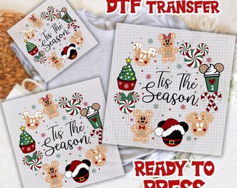 May include: DTF transfer sheets featuring a festive design with gingerbread people, Mickey Mouse ears, candy canes, and Christmas trees. The text "Tis The Season" is displayed on the sheets. Ready to press.