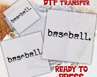 May include: Three white square papers with the word "baseball" printed in black. The papers are on a light gray shirt. The words "DTF TRANSFER" and "READY TO PRESS" are in red.