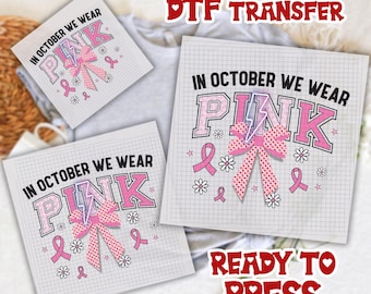 May include: DTF transfer sheets with the text "IN OCTOBER WE WEAR PINK" in pink and black. The design includes a pink bow, ribbons, and flowers. The words "READY TO PRESS" are also visible.