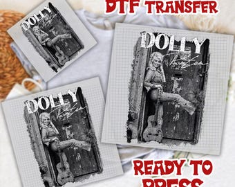 May include: A black and white DTF transfer featuring a graphic of Dolly Parton leaning against a door while holding a guitar. The text reads DOLLY PARTON. The design is printed on a grid background, and the words DTF TRANSFER READY TO PRESS appear in red.