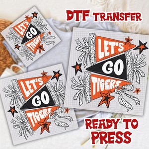 May include: DTF transfer sheets with a pennant design that says "Let's Go Tigers" in orange, black, and white. The sheets have a grid background and star and ribbon accents. The words "Ready to Press" are also visible.