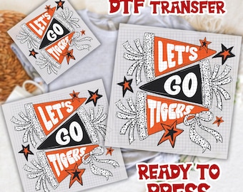 May include: DTF transfer sheets with a pennant design that says "Let's Go Tigers" in orange, black, and white. The sheets have a grid background and star and ribbon accents. The words "Ready to Press" are also visible.