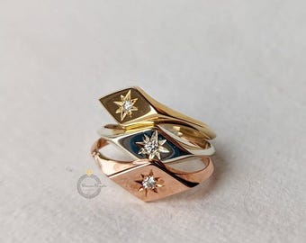 Puede incluir: Tres anillos apilados en oro, plata y oro rosa. Cada anillo presenta un diseño de estrella con diamantes en una cara en forma de diamante. Los anillos se muestran sobre una superficie blanca.
