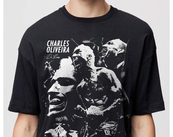 May include: Black t-shirt featuring a grayscale image of Charles Oliveira, with his name and signature printed on the front. The design includes multiple action shots of the fighter. The shirt has a crew neck and short sleeves.