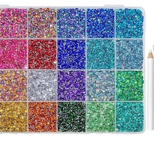 May include: A clear plastic organizer filled with colorful rhinestones in various shades. Includes a tube of B-7000 glue, a white pencil, and a pair of tweezers. The rhinestones are arranged in a grid pattern, offering a wide array of colors.