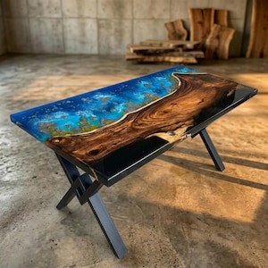 May include: A rectangular wooden table with a blue and brown epoxy resin top. The table has a dark metal base with an X-shaped design. The resin top has a vibrant blue color with a design that resembles an ocean scene.