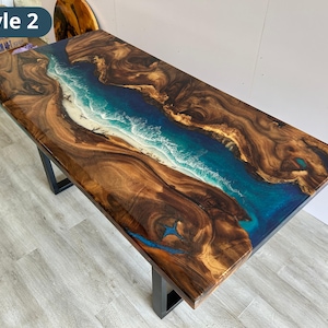Puede incluir: Una mesa rectangular de madera con dise&ntilde;o de r&iacute;o. La mesa presenta una veta de madera marr&oacute;n oscuro con un r&iacute;o de resina azul y blanco que fluye por el centro. La mesa est&aacute; soportada por patas de metal negro. El texto "Style 2" est&aacute; en la esquina superior izquierda.