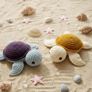 May include: Two crocheted sea turtles, one purple and blue, the other yellow and cream, rest on sand. Pink starfish, seashells, and small stones surround them. The turtles have detailed shells and flippers, creating a beachy theme.
