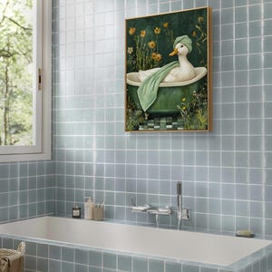 Puede incluir: Una obra de arte enmarcada representa un pato blanco relaj&aacute;ndose en una ba&ntilde;era verde, con una toalla y un turbante verdes. El fondo presenta flores amarillas y vegetaci&oacute;n. La obra est&aacute; situada sobre un fondo de paredes de azulejos azules, lo que sugiere un ba&ntilde;o.
