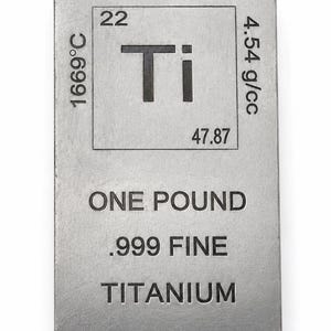 May include: A rectangular silver-colored titanium bar featuring the periodic table symbol Ti, atomic number 22, atomic weight 47.87, melting point 1669°C, and density 4.54 g/cc. The text reads ONE POUND, .999 FINE, and TITANIUM in black lettering.